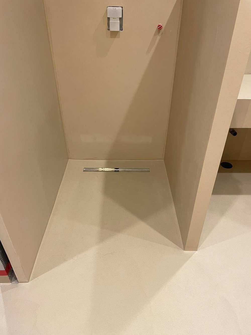 Seamless microcement shower floor falling to a linear drain, with no upstand and no tile joints