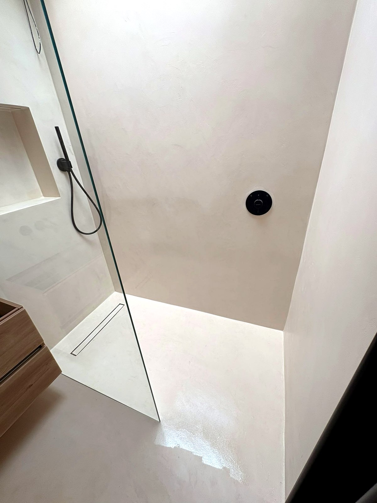 Finished walk-in shower with frameless glass screen and slim linear drain in cream microcement, loft ensuite installation UK